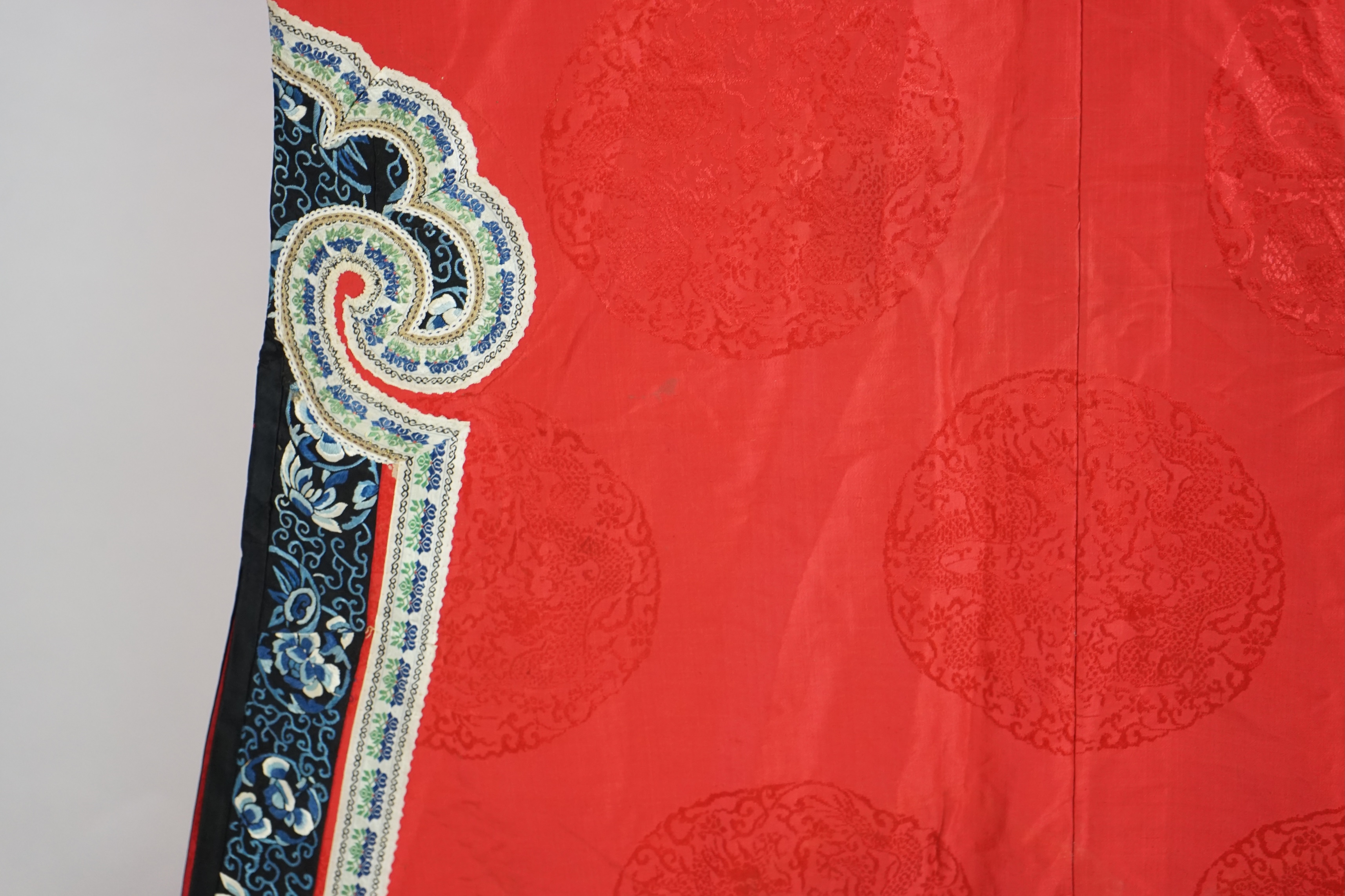 A late 19th century Chinese Manchu ladies red silk damask robe, with black and blue silk embroidered borders, ornately edged cream floral silk braiding, length from neck (back) to bottom edge 132cm long. Condition - stai